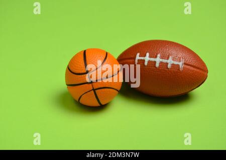 Balles miniatures de football américain et de basket-ball sur un arrière-plan vert Banque D'Images