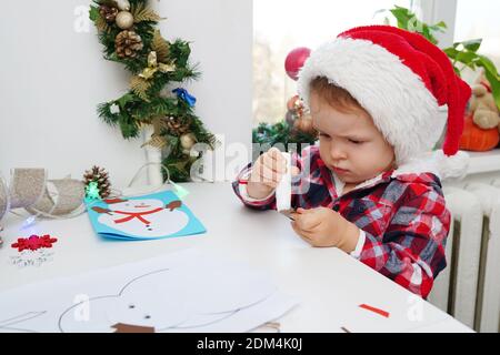 Enfant fille dans chapeau de père Noël faisant carte de noël à partir de papier Banque D'Images