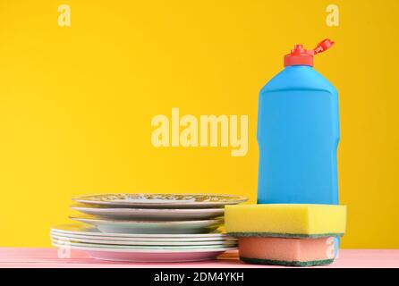 Une bouteille de vaisselle, des éponges, des ustensiles sur une table en bois de couleur pastel sur un fond de mur jaune, un espace de copie Banque D'Images