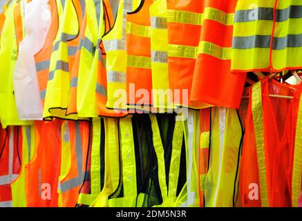 Collection de tissus réfléchissants de sécurité, orange et jaune, suspendus dans des gilets de rangée. Banque D'Images