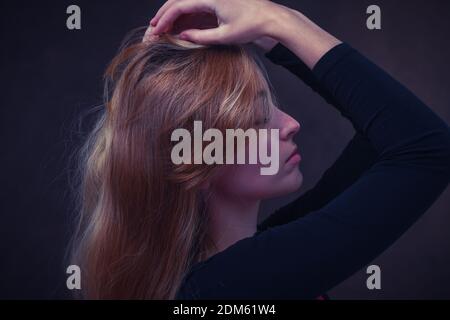 Jeunes femmes naturellement belles (20 ans) avec de longs cheveux blonds vue latérale studio lumineux portrait montrant l'émotion avec les mains sur le dessus de la tête. Banque D'Images