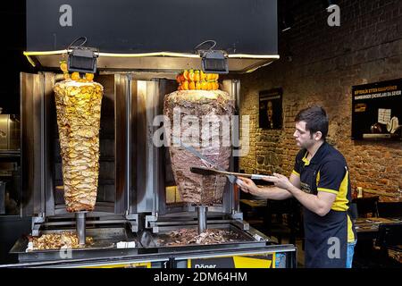 Istanbul, Turquie - 14 février 2020: Le vendeur de kebabs de doner le plat contenant de la viande cuite sur une broche verticale. Banque D'Images