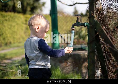 Garçon se lavant les mains sous le robinet du jardin Banque D'Images