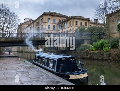 Un bateau étroit sur le canal Leeds Liverpool à Saltaire, Yorkshire. Salts Mill est en arrière-plan. Banque D'Images