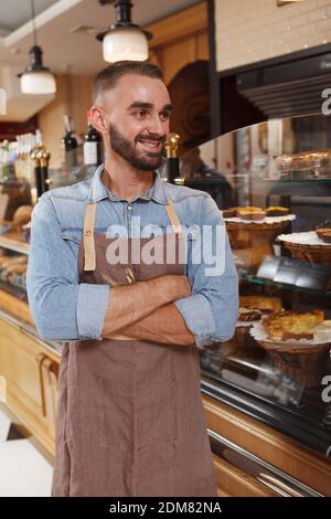 Plan vertical d'un boulanger mâle portant un tablier en appréciant le travail à sa boulangerie Banque D'Images