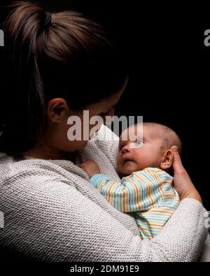 Vue latérale de Happy MOM cuddling adorable nouveau-né et profitez de moments de maternité sur fond noir Banque D'Images