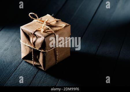 Emballage enveloppé dans du papier kraft et attaché avec une corde arrière-plan en bois noir Banque D'Images