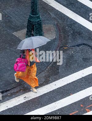 Vue depuis le dessus de la femme en robe colorée avec parasol traversant la rue de la ville par un jour de rêve, tandis que les vêtements lumineux contrastent fortement avec le pavé sombre. Banque D'Images