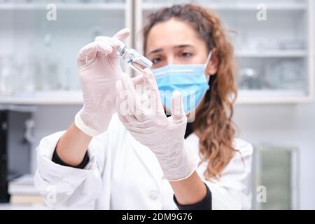 Une jeune scientifique féminine portant un masque facial tenant un flacon de vaccin contre le coronavirus. Développement du vaccin Covid-19. Banque D'Images