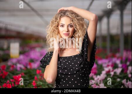 jeune belle fille se tient dans un arrangement de fleur parmi les fleurs et regarde dans la caméra Banque D'Images