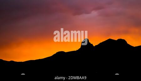 Coucher de soleil à travers les nuages avec des rayons de lumière. Violet et orange vif avec silhouette de montagne noire à l'horizon. Banque D'Images