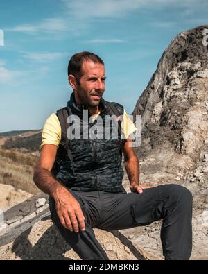 Portrait d'un jeune homme avec un sac à dos et un volcan de boue en arrière-plan, photo prise en Roumanie Banque D'Images