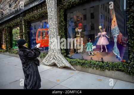 New York, États-Unis, 16 décembre 2020. Une femme portant un manteau de fourrure porte un masque de visage pendant qu'elle photographie les fenêtres décorées de Noël du département de Saks Fifth Avenue Banque D'Images