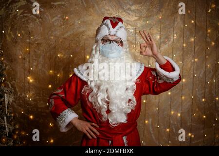 Le Père Noël pose dans un masque sur un fond de mur avec une guirlande montre différents gestes avec ses mains Banque D'Images