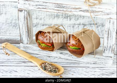 Hamburger au saumon sain avec avocat et tomate servi dans l'artisanat papier sur fond en bois Banque D'Images
