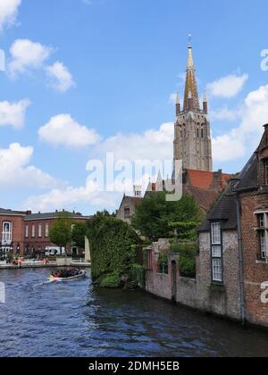 BRUGES, BELGIQUE - 10 mai 2019: Belgique, Bruges, ,10 mai 2019, 1.30:00, Canal avec bateau touristique, bâtiments en brique rouge en partie avec usine d'escalade Banque D'Images