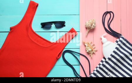 Vêtements et accessoires pour femmes pour se détendre sur la plage sur fond pastel en bois. T-shirt, sac de plage, écran solaire, lunettes de soleil, vue du dessus, plat l Banque D'Images