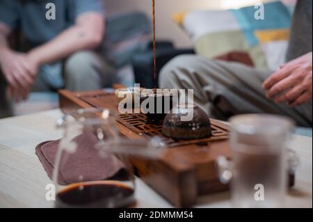 Les mains des hommes versent le thé ambré parfumé dans un bol en verre. Cérémonie du thé et dégustation dans le style chinois traditionnel Banque D'Images