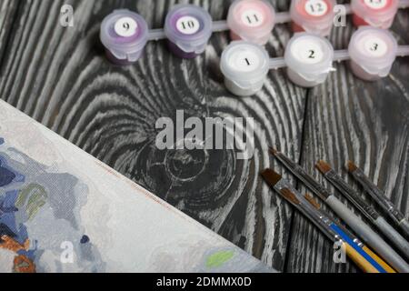 Peindre par numéro les pinceaux et les peintures. À proximité se trouve un fragment d'une image peinte. Sur les planches de pin noir. Banque D'Images