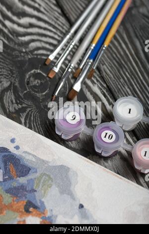 Peindre par numéro les pinceaux et les peintures. À proximité se trouve un fragment d'une image peinte. Sur les planches de pin noir. Banque D'Images