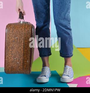 Femme avec jeans et baskets tenant dans sa main valise rétro sur fond de papier multicolore. Banque D'Images