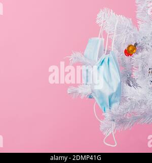 gros plan de quelques masques jetables bleus suspendus des branches d'un arbre blanc de noël, sur fond rose Banque D'Images