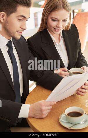 Offre réussie. Photo verticale d'un homme d'affaires et d'une femme d'affaires travaillant avec des papiers au café local Banque D'Images