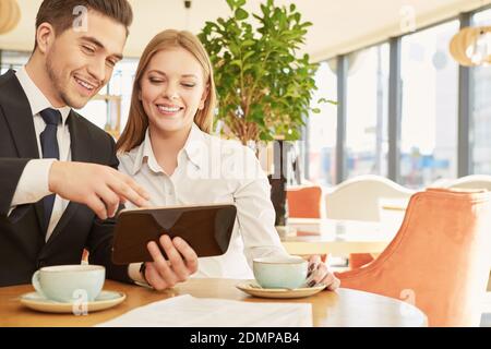 Jetez un coup d'œil. Jeune homme d'affaires souriant souriant montrant joyeusement quelque chose dans sa tablette à son beau collègue souriant Banque D'Images
