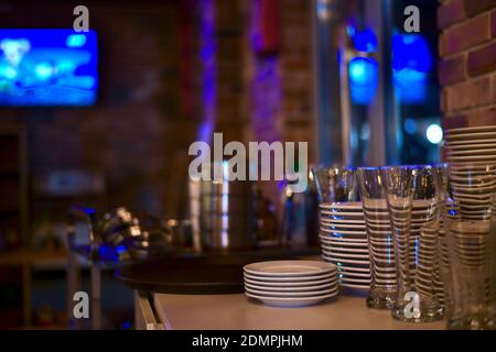 Stacks of a clean shiny utensils made of steel, ceramics and glass. On the countertop of the bollard near the brick wall, in a room with subdued light Stock Photo