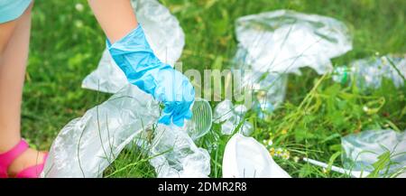 La main de l'enfant nettoie le parc des ustensiles en plastique dans l'herbe dans le parc Banque D'Images