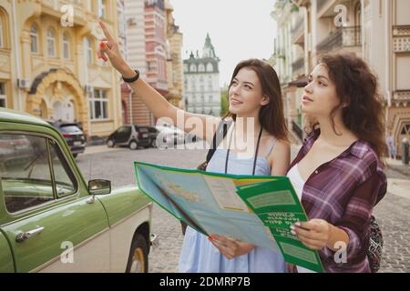 Two lovely young women looking around on the street of an old city, using map. Female friends traveling together, sightseeing in the town Stock Photo