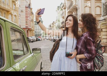 Jeunes femmes adorables et heureuses qui prennent des selfies tout en faisant du tourisme dans la ville, un espace de copie. Des amies joyeuses qui apprécient de voyager ensemble en été Banque D'Images