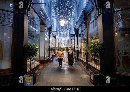 Two people wearing face masks and carrying shopping bags walk through Mogan Arcade in Cardiff, Wales, during the christmas period. Banque D'Images