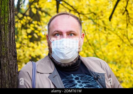 Portrait of a mature man wearing surgical mask in the city park, outside in a sunny day Stock Photo