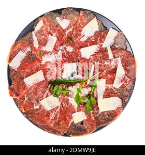 Vue de dessus d'une portion de carpaccio (filet de bœuf cru finement tranché) décorée de parmesan, d'arugula et de câpres sur une assiette noire isolée sur fond blanc Banque D'Images