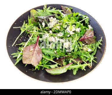 salade fraîche de bettes et d'arugula avec du fromage bleu, du poivre et de l'huile d'olive sur une assiette brun foncé isolée sur fond blanc Banque D'Images