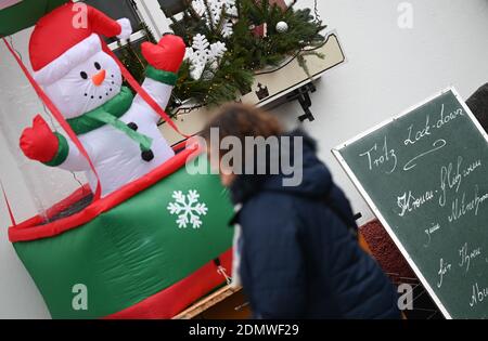 Seligenstadt, Allemagne. 17 décembre 2020. Une femme se tient devant un restaurant de la vieille ville, devant lequel un bonhomme de neige gonflable et un panneau indiquant « cadenas à cadenas » ont été placés. Dans la lutte contre le coronavirus, la vie publique est fermée pour la deuxième fois cette année. Credit: Arne Dedert/dpa/Alay Live News Banque D'Images