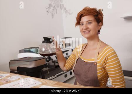 Coupe courte d'un barista féminin portant un noir fraîchement préparé café dans une casserole en verre Banque D'Images
