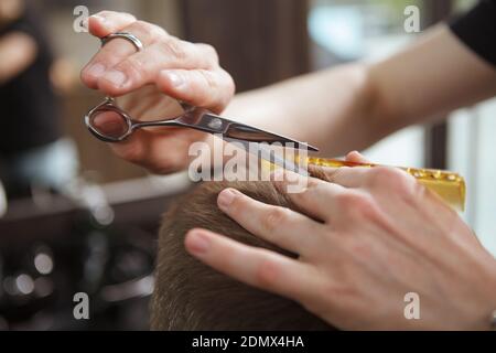 Gros plan d'un coiffeur utilisant des ciseaux au travail, donnant à un client mâle une nouvelle coupe de cheveux Banque D'Images