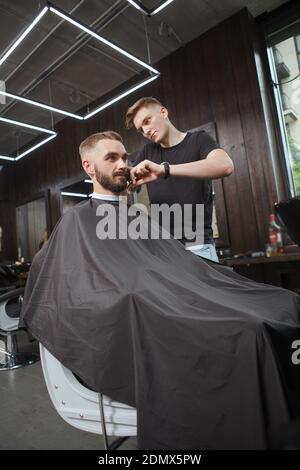 Photo verticale d'un beau homme qui obtient une nouvelle coiffure par le barbier professionnel au barbershop Banque D'Images