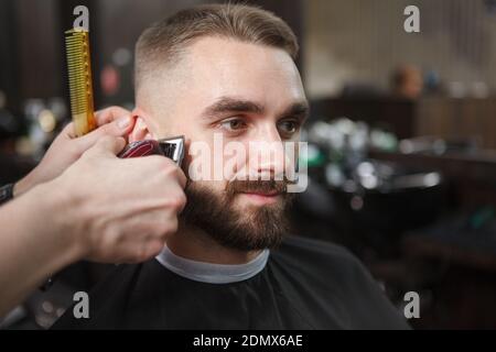 Gros plan sur un bel homme barbu qui se fait coiffer taillé par un barbier professionnel Banque D'Images