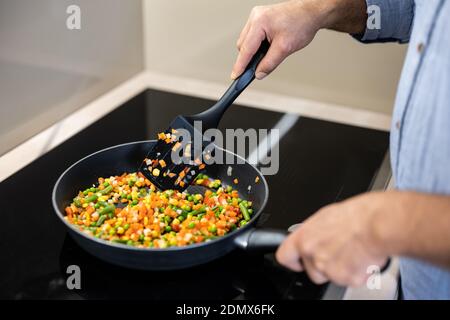 Rasez les légumes de couleur dans une casserole. Main de l'homme adulte tenant la spatule et le plat à mélanger. Concept d'alimentation saine. Appareils de cuisine modernes. Sain et savoureux Banque D'Images