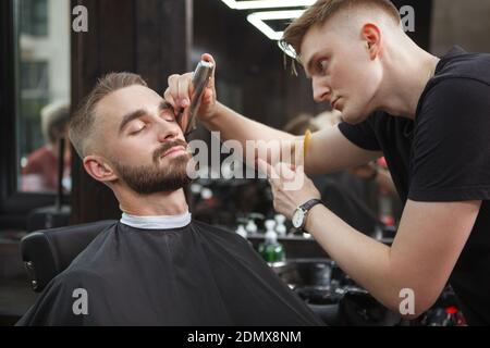 Beau homme qui a l'air détendu tout en radoutant sa barbe coiffeur Banque D'Images