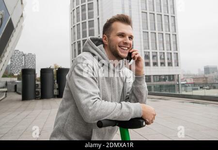 Un homme attrayant avec une barbe raconte à son ami au téléphone la commodité de louer un véhicule électrique. Concept de transport écologique. Décontracté Banque D'Images