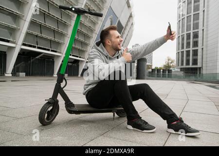 Guy aime le nouveau service de location de scooter électrique. Il passe des appels vidéo à ses amis et parle des avantages de cette application pour smartphone. Man si Banque D'Images