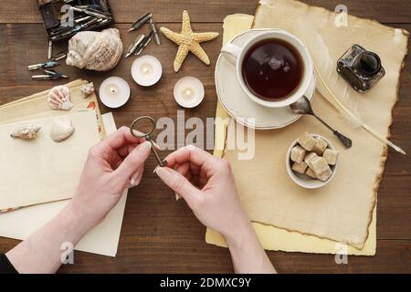La femme tient une vieille clé dans ses mains. Sur la table sont des feuilles de papier vierges, des vieilles lettres et une tasse de thé. Souvenir du passé lointain. Banque D'Images