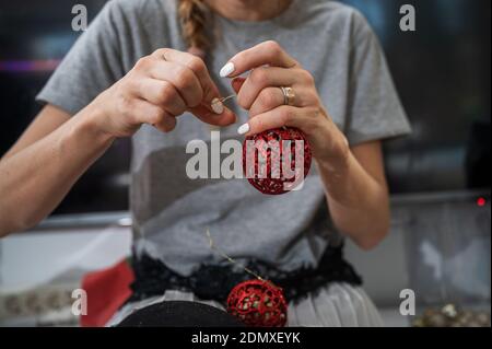 Closeup view of a woman tying golden string to a shiny red christmas holiday bauble. Banque D'Images