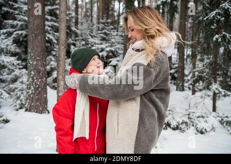 Une jeune mère ajuste le foulard de son fils lors d'une matinée glacielle dans les bois. Banque D'Images