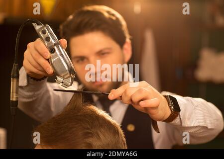 Mise au point sélective sur un coupe-herbe dans les mains de coiffeur professionnel donnant une coupe de cheveux à son client travaillant à le service de barbershop de barbering co Banque D'Images