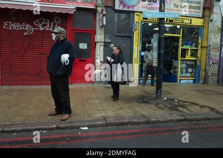 Un membre du public porte un masque comme lui Attend un bus sur New Cross Road pendant le Pandémie de coronavirus Banque D'Images